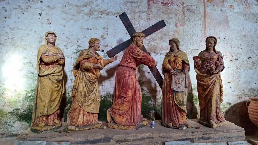 Slow forward shot of painted wooden statues depicting Jesus carrying cross with surrounding figures in private chapel, Mayenne.