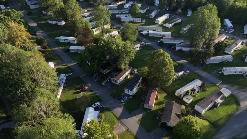 Peaceful low income housing with mobile trailer homes in idyllic suburbia of American Town. Late summer with colored trees at sunset. Aerial view.