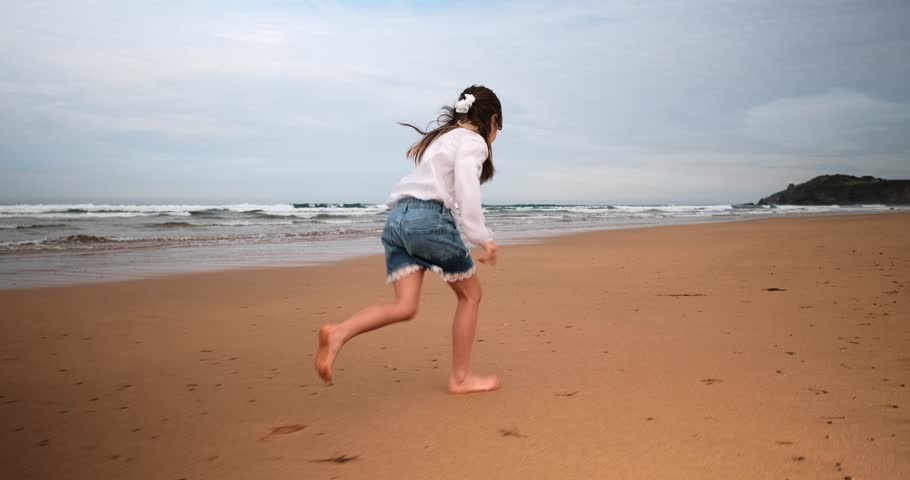 Girl running along shoreline on sandy beach, slow-motion wide