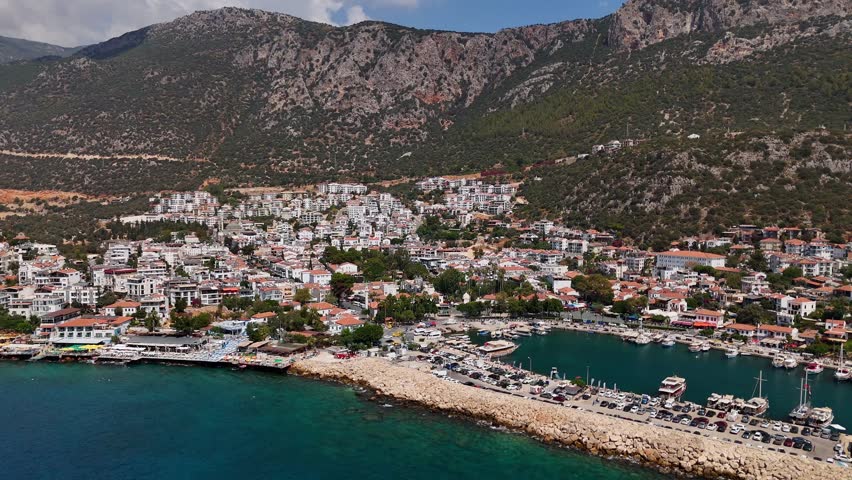 Aerial view of Kas, Turkey a beautiful coastal town surrounded by green hills and the Mediterranean Sea, with white houses, marina, and boats along the shore.