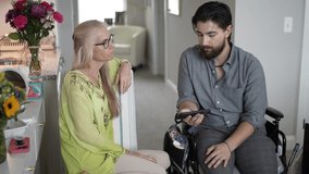 A young man in a wheelchair interacts with his mother, sharing happy memories on his smartphone in their cozy living room, creating special moments together. - Powered by Shutterstock - Get 15% off with code: PIKWIZARD15