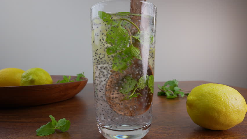 A close-up of a tall glass of refreshing detox water with lemon, mint, and chia seeds on a wooden table