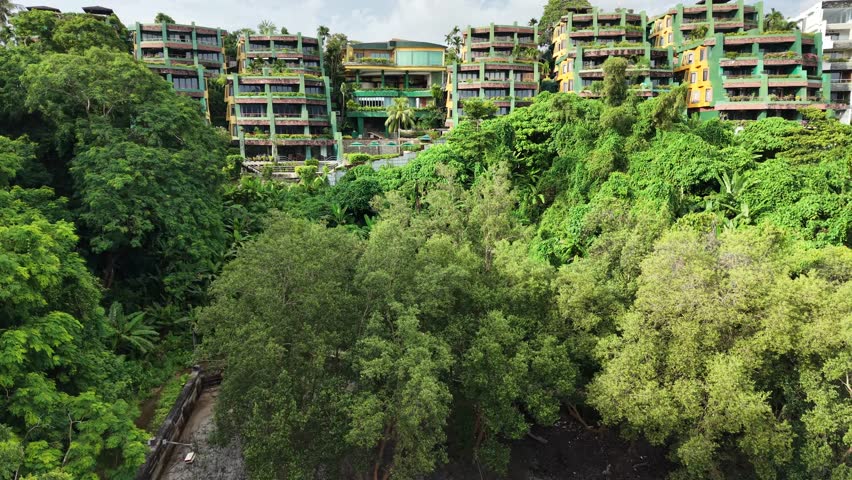 Aerial view of green eco-style buildings and hotels near the coastline, overlooking the beach and sea on a sunny day. High quality 4k footage