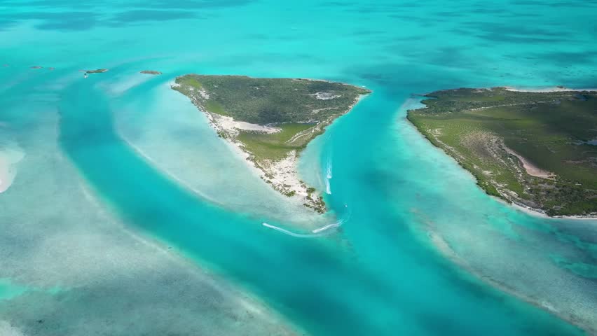 Stunning aerial drone footage of a tropical island paradise in the Bahamas. Speedboats navigate through a channel of vibrant turquoise water, surrounded by beautiful white sandbanks and lush islands.