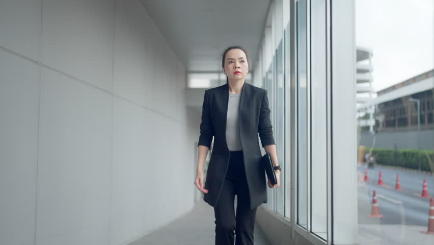 Asian businesswoman in smart casual outfit rushing through office hallway while checking time on smartwatch. Concept of urgency, pressure, and time management. - Powered by Shutterstock - Get 15% off with code: PIKWIZARD15