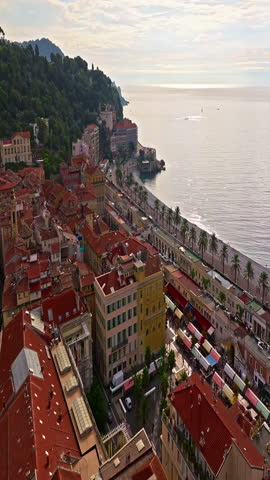  Aerial view of bustling beachfront promenade on sunny day. Beautiful panorama in Nice, France. Palm trees, old houses in old town azure sea and green hills. Summer in French Riviera