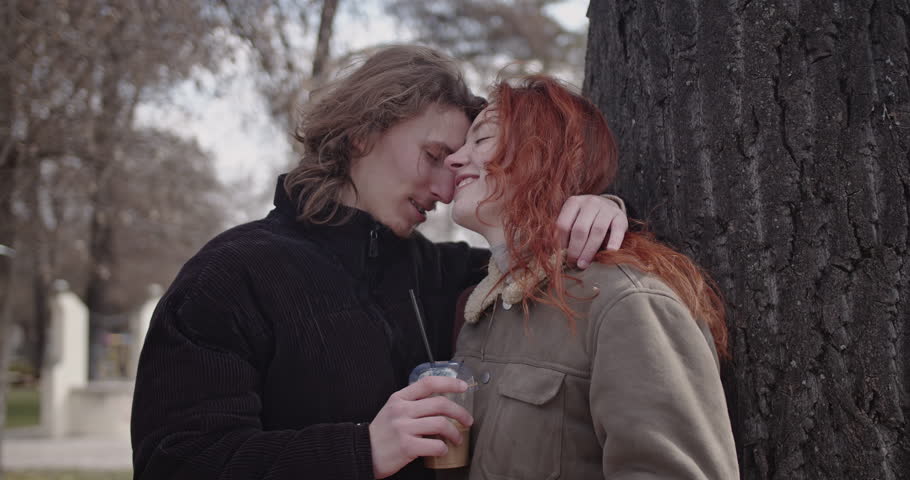 A young couple shares a romantic moment in a park, kissing and enjoying each other