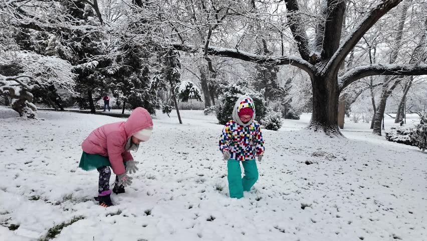Two little girls playing games and having fun, having a snow ball fight in the snow. Happy children play snowballs