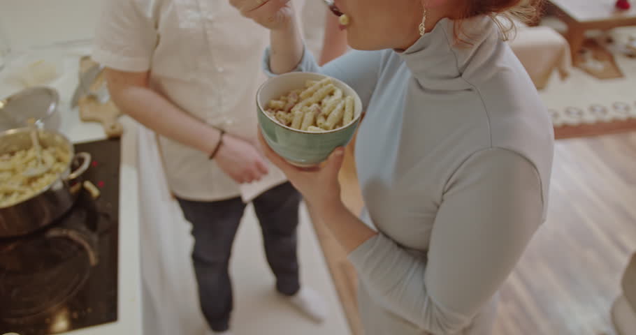A woman tastes a delicious pasta dish prepared by a man in a chef