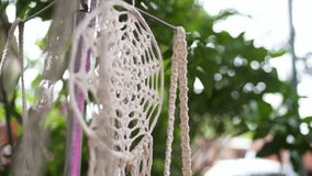 A beautiful close-up of a handmade dreamcatcher, intricately woven in a crochet style. It hangs outdoors, gently moving, with a soft, out-of-focus background of green foliage. - Powered by Shutterstock - Get 15% off with code: PIKWIZARD15