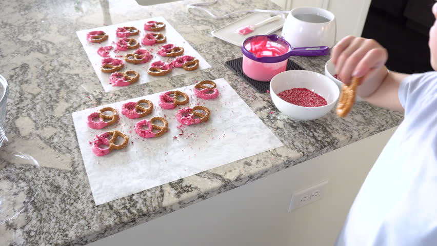 With focused attention, this budding culinary artist dips pretzels into a pot of melted chocolate, creating sweet delights in the warmth of a well-lit home kitchen.