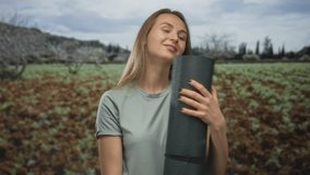 Young woman holding yoga mat in green field under cloudy sky, wearing casual clothes, represents outdoor relaxation and healthy lifestyle in natural setting with rustic background. - Powered by Shutterstock - Get 15% off with code: PIKWIZARD15