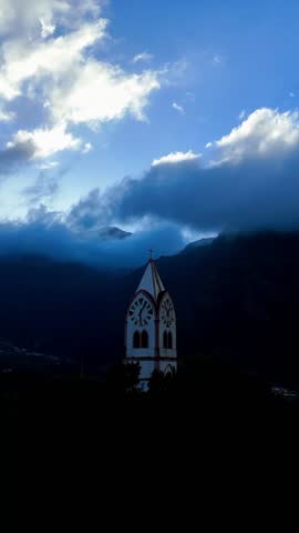 A vertical shot of a church steeple rising from a dark valley under a dramatic, cloudy sky