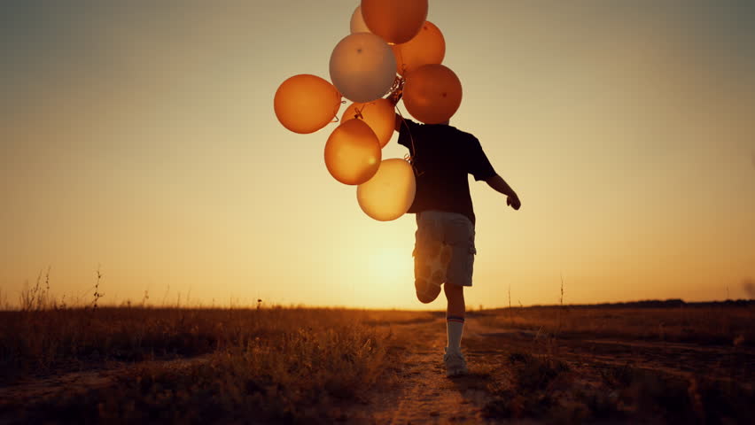 Feel happiness and joy, little child having fun in nature, running with balloons . Slow motion back view with carefree boy enjoying simple life in countryside, human and nature, positive emotion