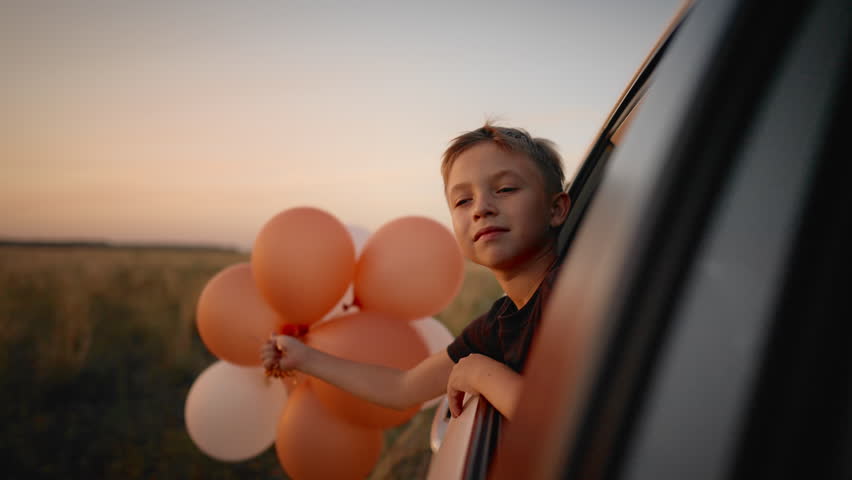 Portrait of cute 6-years-old boy with balloons traveling by car with family. Weekend trip and celebration of birthday party in nature, little dreamer dreaming of future, enjoy simple life and summer