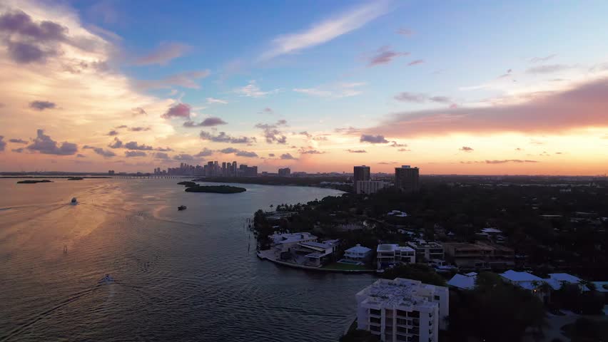 Aerial view of Biscayne Bay reveals the Miami skyline under a sky streaked with orange and blue, reflecting on the water