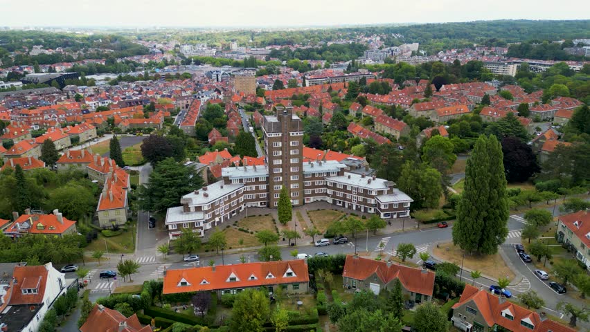 Aerial view of buildings with orange roofs nestled among lush green trees, creating a vibrant contrast in the landscape, Watermael-Boitsfort, Brussels, Belgium.
