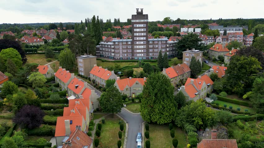 Aerial view of a tall building with a tower surrounded by verdant trees and houses with orange roofs, creating a contrasting urban landscape, Watermael-Boitsfort, Brussels, Belgium.