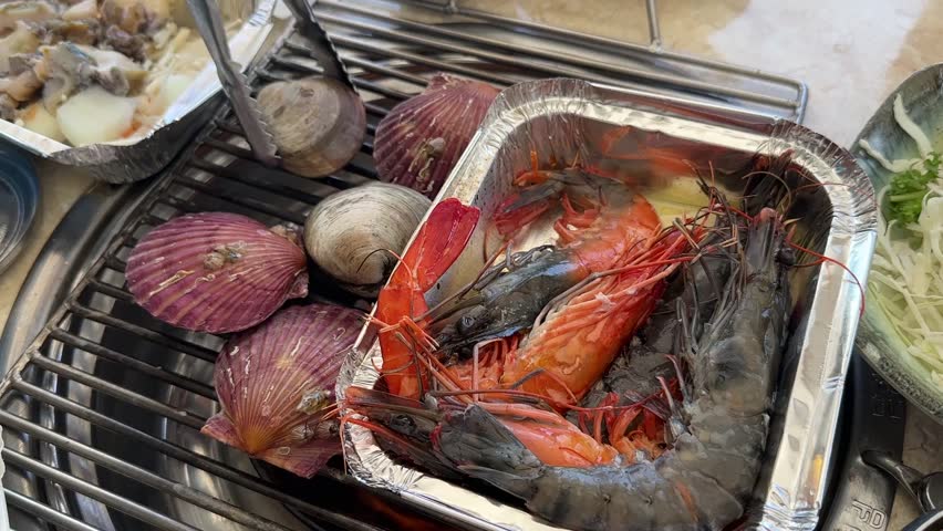 Famous restaurant in Haeundae Beach, Busan, South Korea. Server cooking fresh shellfish (shrimp, scallops, and clams) over a hot charcoal grill.