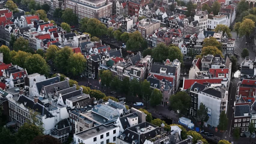 Drone dolly right across Amsterdam city center at golden sunrise, rooftops and canals, city block urban textured backdrop