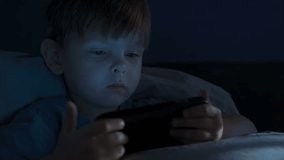 A young boy lies in bed at night closely watching a glowing smartphone screen, playing mobile games or watching videos, illustrating gadget addiction, digital overuse, and late-night screen time. - Powered by Shutterstock - Get 15% off with code: PIKWIZARD15