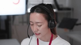 Young Asian call center woman wearing headset and microphone while working at computer in modern office. Professional customer support representative providing online assistance, technical help - Powered by Shutterstock - Get 15% off with code: PIKWIZARD15