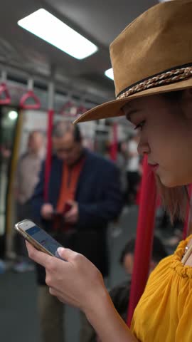 Young beautiful asian woman interior metro hold in the hands the phone. A passenger wear a hat using smartphone in subway to do some quick text messaging in Hongkong