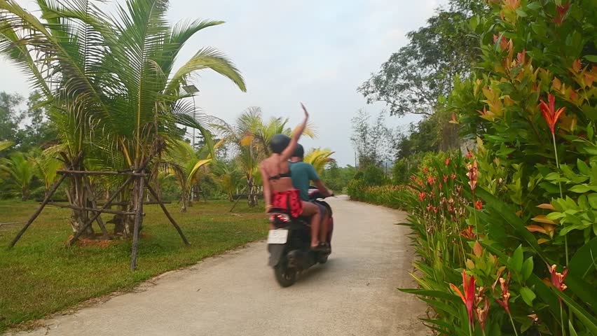 Vietnam - 16th march, 2024: Young happy caucasian couple e having fun pose on scooter together with palm trees, drive red scooter.Tropical road trip in southeast asia. Couple in love having fun travel