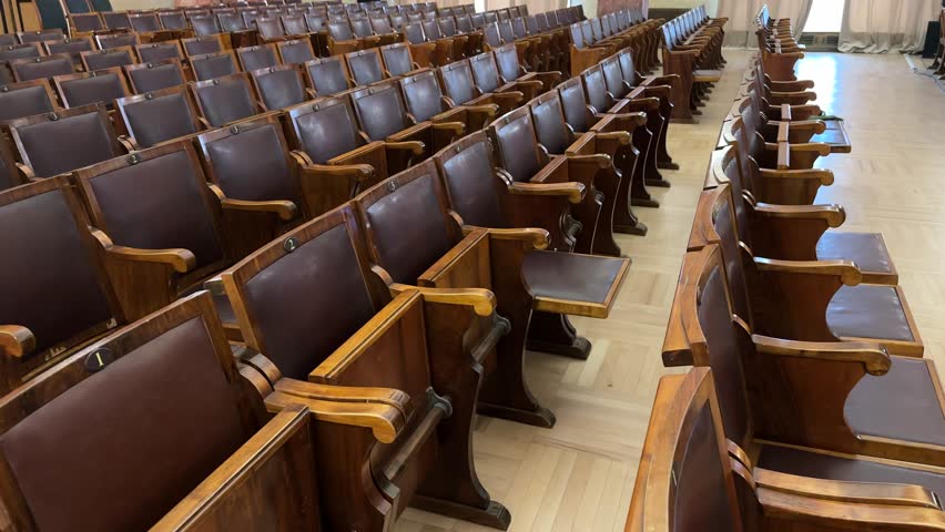 A vintage concert hall featuring wooden seats and parquet flooring in warm brown tones. The interior exudes a classic and nostalgic atmosphere with intricate woodwork and elegant design