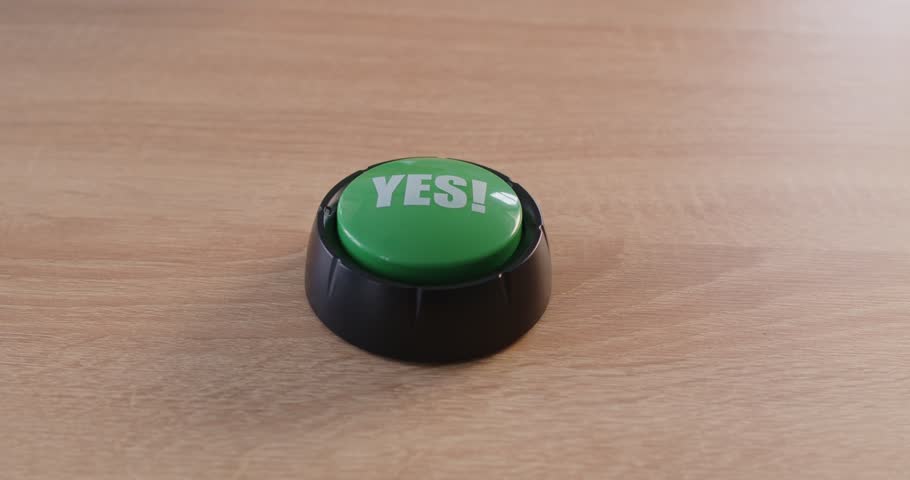 On a wooden desk, a green yes button sits ready as a hand hovers, implying pressing for approval or accept. A hand presses a green yes button. Concept of decision, confirm, choice and action.