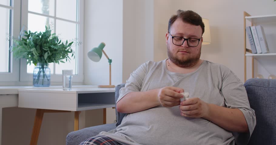 Obese man holds pill and medicine. overweight patient takes water and prepares a tablet for diabetes, following treatment at home. Concept healthcare and chronic illness management.