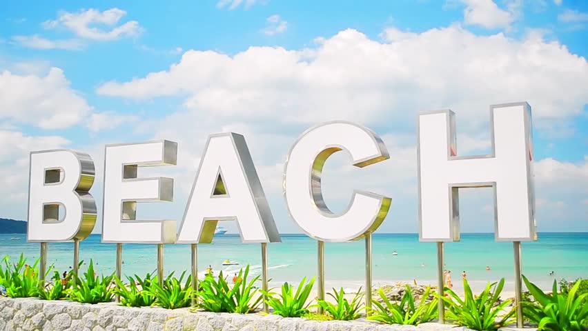 Beach sign under bright blue sky with fluffy white clouds, symbolizing travel, vacation, summer holidays, and seaside destinations.