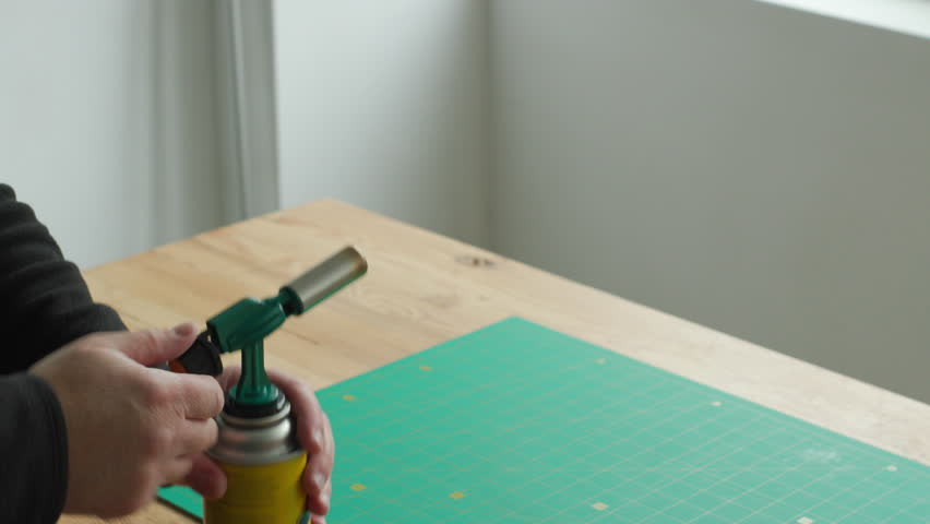 Hand lighting a butane blow torch with blue flame on workbench - close up