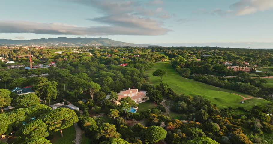 Portugal, Lisbon: Cascais exclusive residential area combining lush green golf course with luxury villas nestled among rich canopy of trees and a distant view of the sea. Aerial view drone panorama