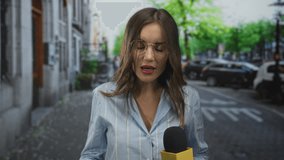 Woman reporter holding microphone in hand gestures with raised palm while speaking on street; news reporting urgency. - Powered by Shutterstock - Get 15% off with code: PIKWIZARD15