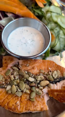 Vertical 4K footage of traditional Norwegian grilled salmon fillet topped with pumpkin seeds, served with cooked potatoes and fresh salad from a restaurant in Norway Bergen fish market. 