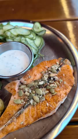 Vertical 4K footage of traditional Norwegian grilled salmon fillet topped with pumpkin seeds, served with cooked potatoes and fresh salad from a restaurant in Norway Bergen fish market. 