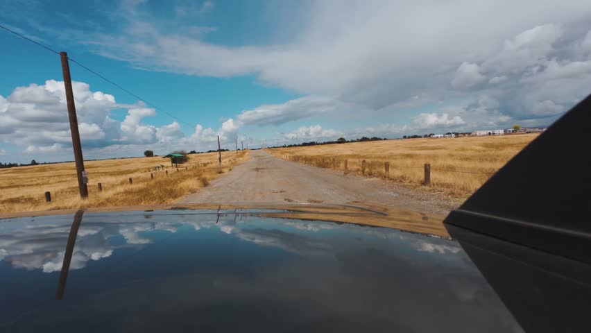 View from back of a car Driving on a Dirt Road Through Golden Dry Grasslands Under a Dynamic sky