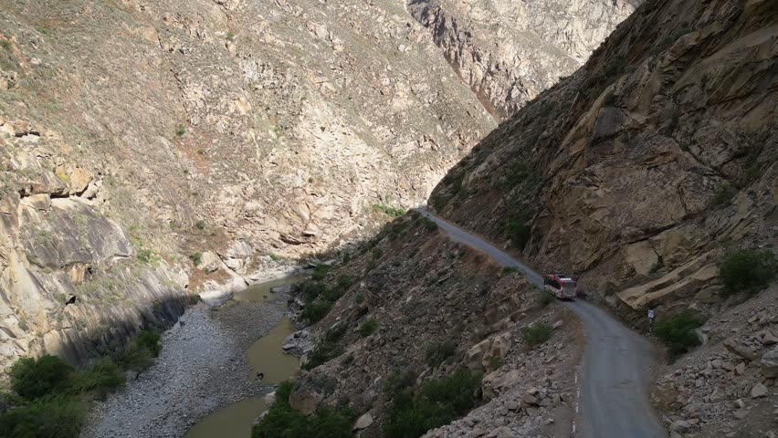 Huaraz, Peru: Aerial footage of drone following bus driving out of tunnel in narrow road of canon del pato. Shot in forward motion showing the narrow road in between two mountains