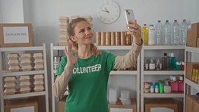 Woman uses hand to take selfie in a warehouse volunteer donation setting, smiling with blonde hair and young face against shelves. - Powered by Shutterstock - Get 15% off with code: PIKWIZARD15