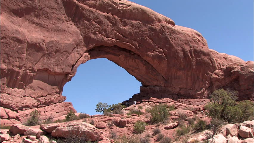 Zoom into rock arch with tourists climbing through it