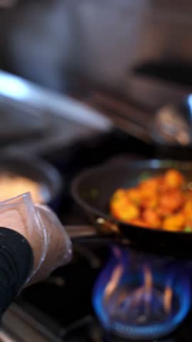 Close-up of spiced potatoes frying in a hot pan over a blue gas flame. Perfect for food promos, restaurant ads, recipe videos, and cinematic kitchen visuals.