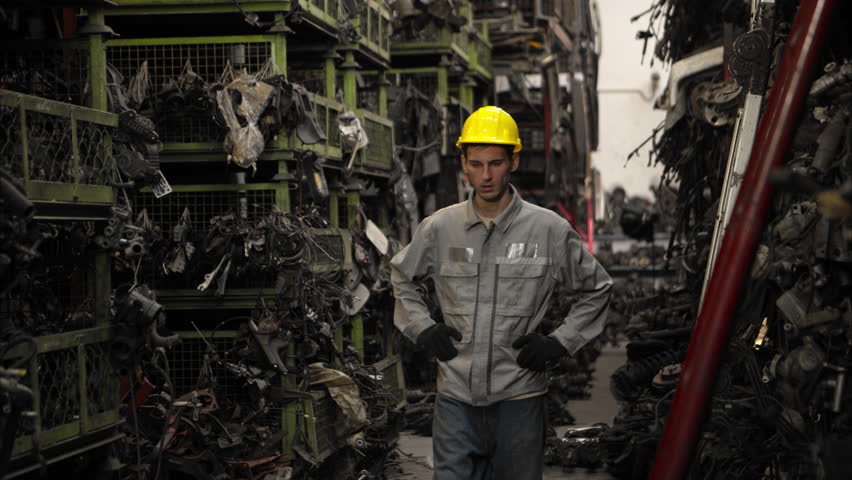 Tired industrial worker wearing safety uniform and gloves wiping sweat from his forehead after hard physical labor in a factory, representing fatigue and exhaustion at work
