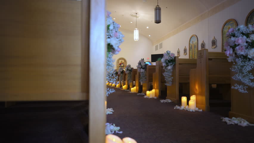 The aisle with floral decorated wooden pews rows and candles on the floor in empty church. Christian cathedral interior decoration for the wedding event