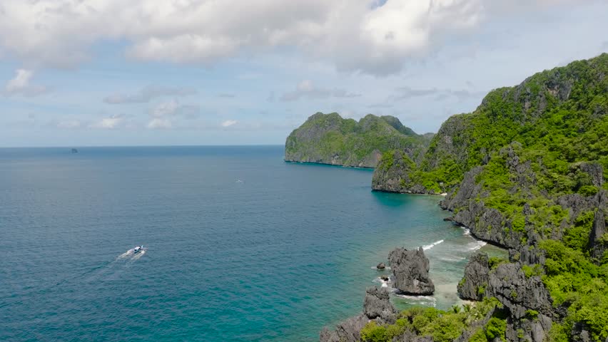 Towering limestone formations draped with lush tropical foliage. Gentle waves caressing the rocky shorelines. El Nido, Philippines.