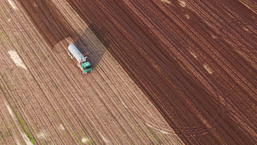 Drone overhead view of manure spreader creating wide brown strip over cultivated field in motion