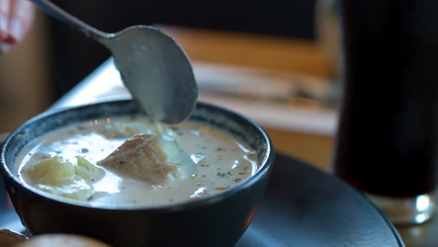 Hand lifts spoonful of creamy fish chowder with potatoes under soft, natural restaurant lighting