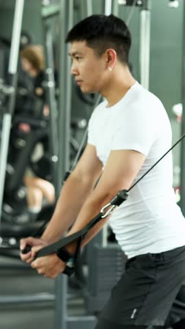Athletic man performs cable chest fly with rope attachments in bright, modern gym, side view.