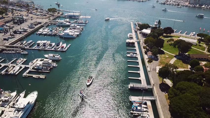 Bird’s eye aerial of Marina del Rey, Los Angeles. The camera tracks laterally from a top down angle across boat slips, docks, and a narrow channel with small craft and sailboats leaving wakes.