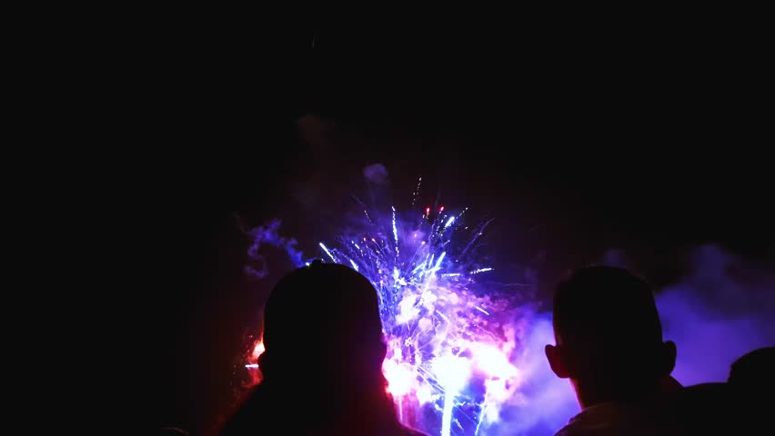 Silhouetted figures of people revealed by the colorful cosmic firework exploding in a dark night sky during a pyrotechnic display